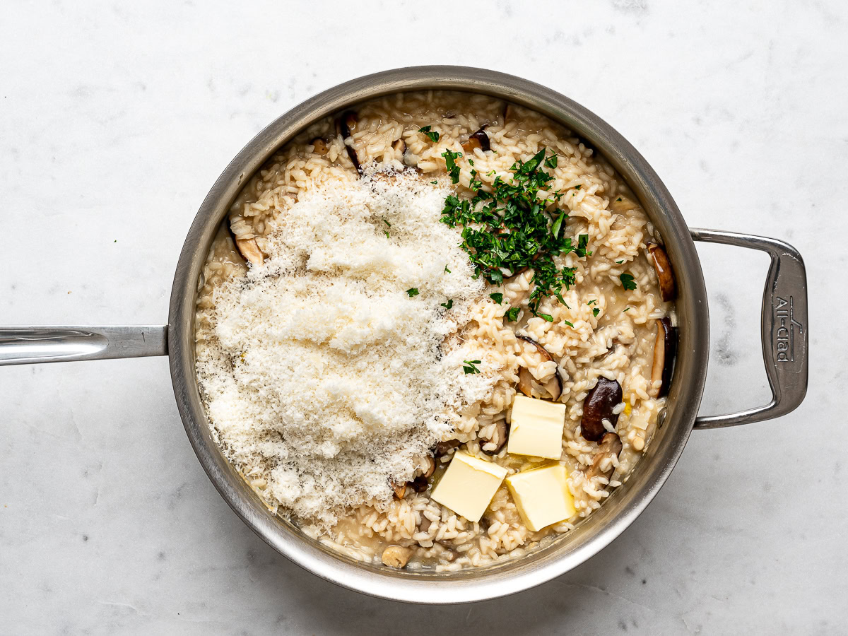 parmesan cheese, butter and parsley being added to the mushroom risotto in the pan