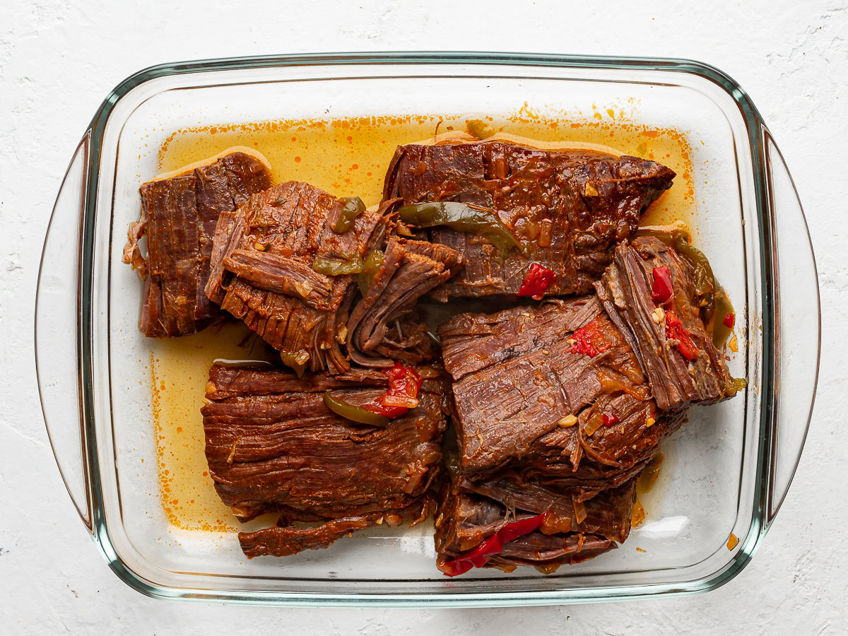 cooked pieces of flank steak in a glass rectangular bowl ready to be shredded