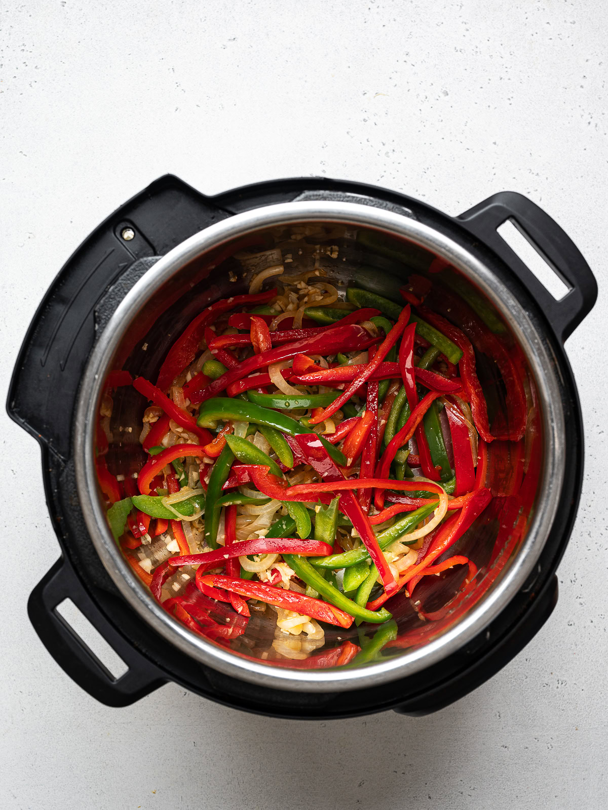 sliced onion and bell peppers sautéing in an Instant Pot