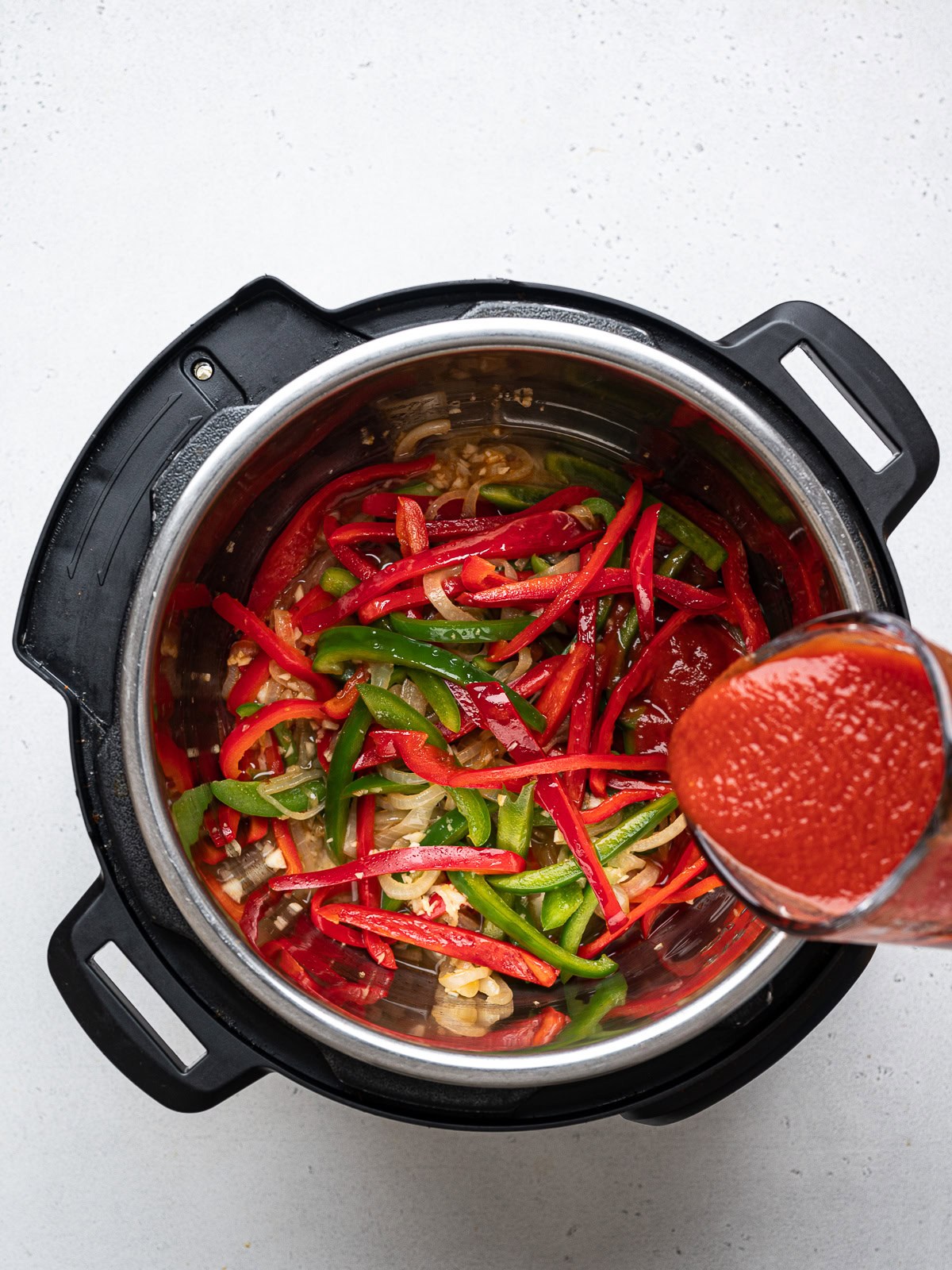 pouring tomato sauce over onion and bell pepper mixture