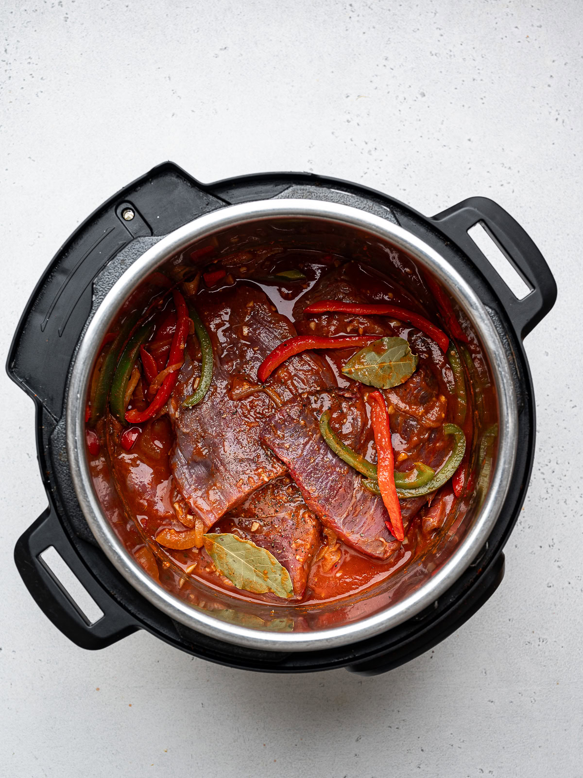 raw flank steak pieces nestled in with onion and bell pepper mixture in the instant pot