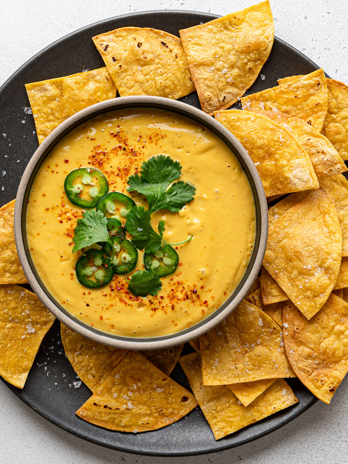 Vegan queso served in a bowl garnished with sliced jalapeño peppers and cilantro and tortilla chips surrounding it