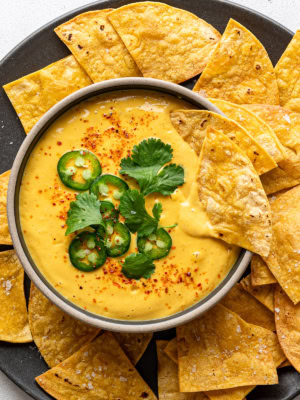 Vegan queso served in a bowl garnished with sliced jalapeño peppers and cilantro and tortilla chips surrounding it