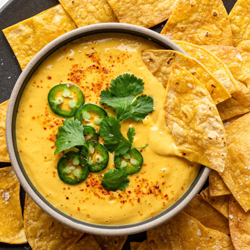 Vegan queso served in a bowl garnished with sliced jalapeño peppers and cilantro and tortilla chips surrounding it