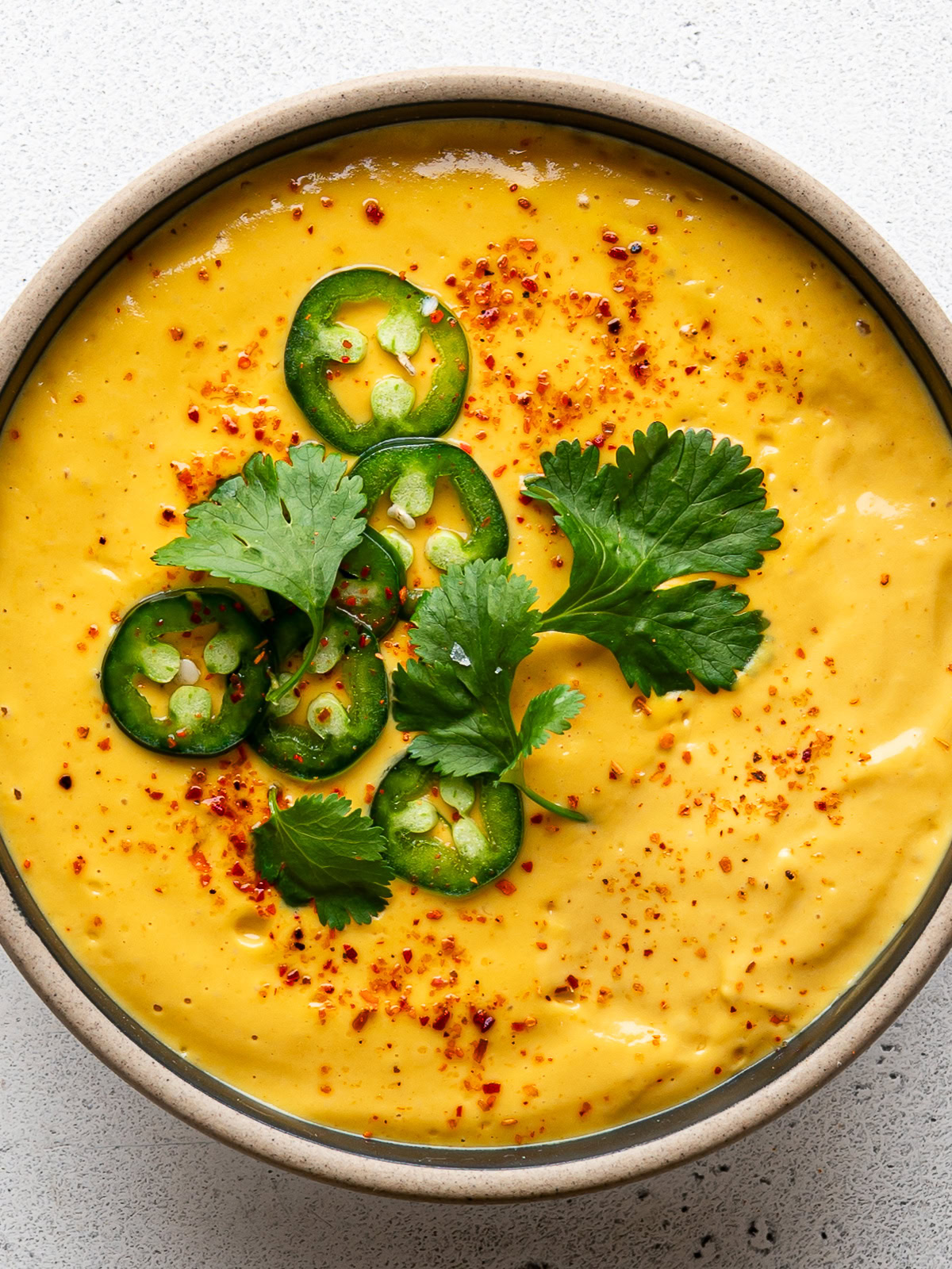 top-view of queso sauce served in bowl and garnished with jalapeño peppers and cilantro