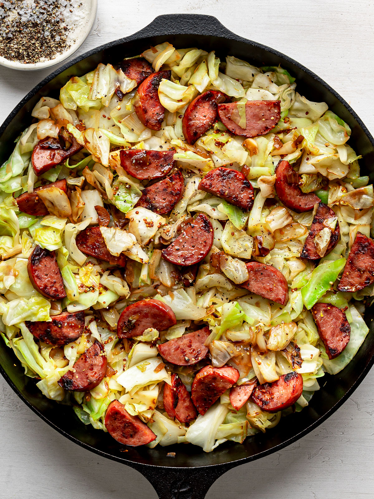 The finished dish of Sautéed cabbage and sausage in a black skillet. 