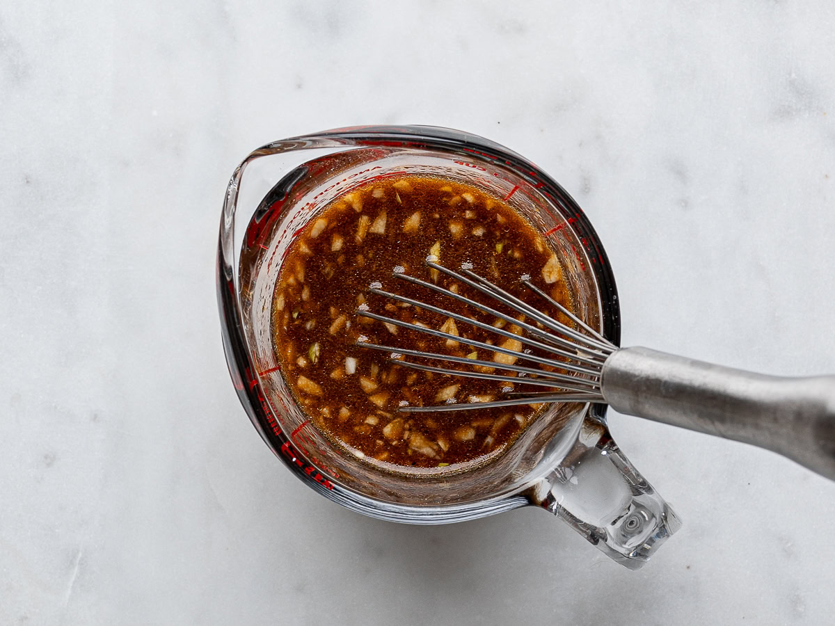 Mixed teriyaki sauce in glass measuring jar with a whisk.