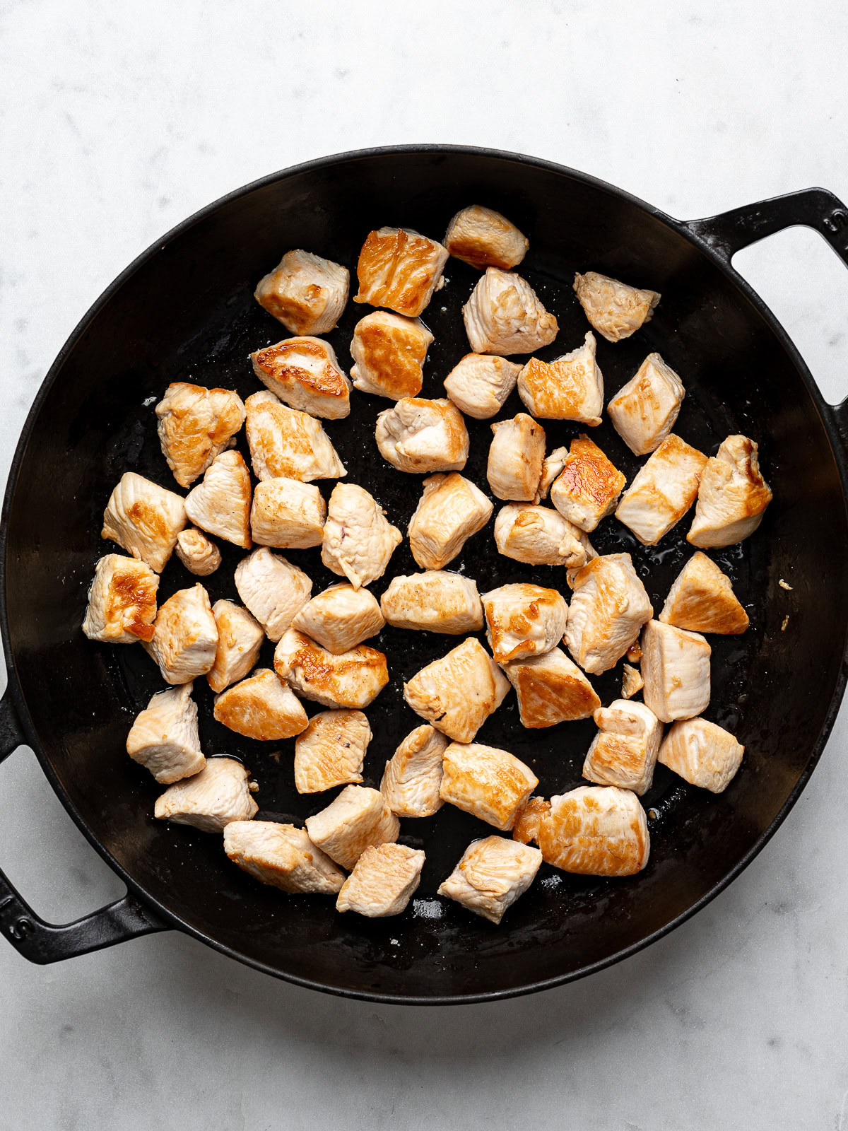 Cooked cubed chicken pieces in black skillet.