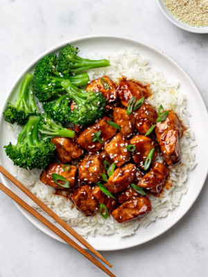 Teriyaki chicken served over fluffy white rice on a white plate with steamed broccoli on the side