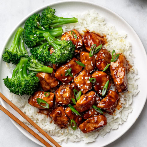Teriyaki chicken served over fluffy white rice on a white plate with steamed broccoli on the side