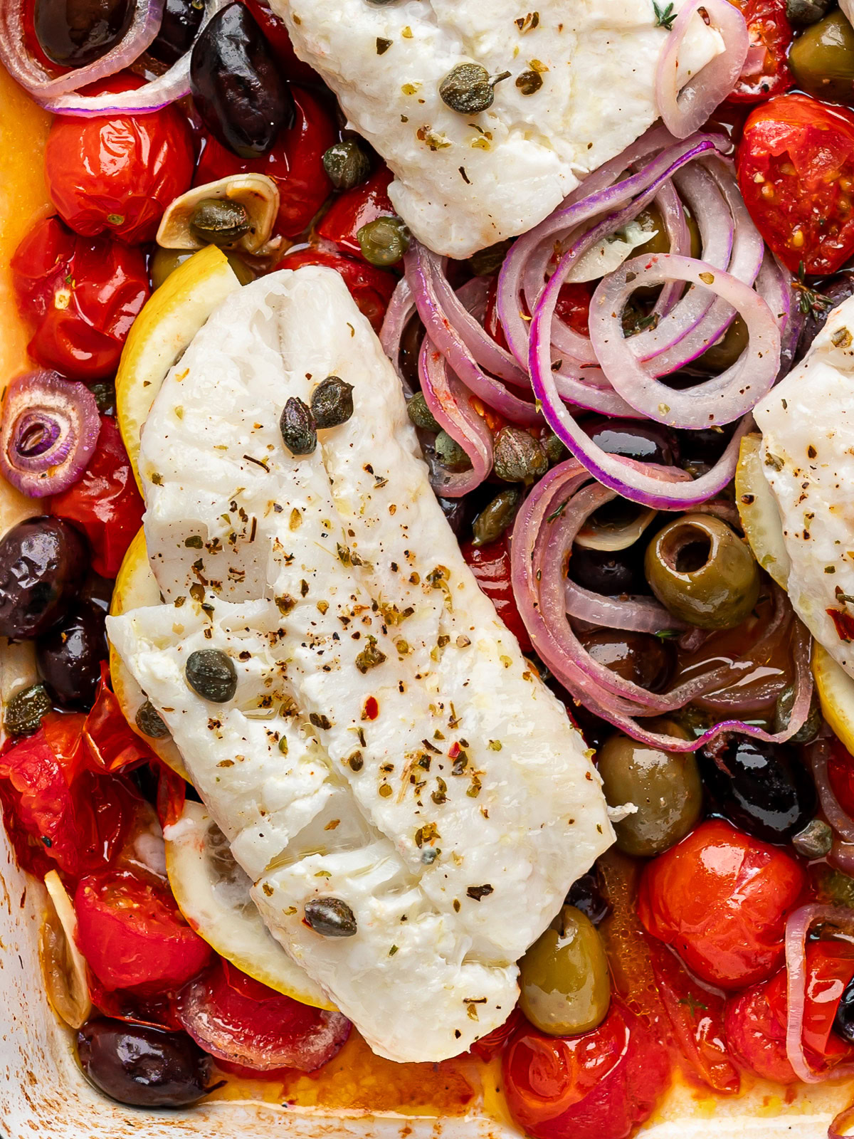 closeup of one Baked cod fillet on top of  cherry tomato mixture in baking dish.