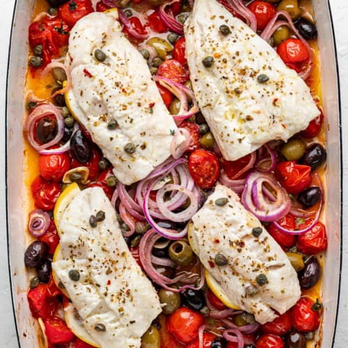 4 cod fillets on top of a burst cherry tomato sauce in a baking dish.