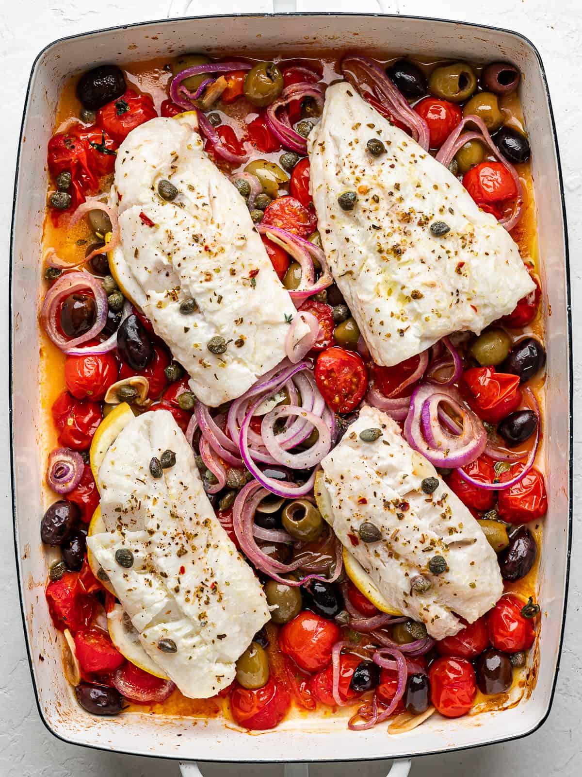 4 cod fillets on top of a burst cherry tomato sauce in a baking dish. 