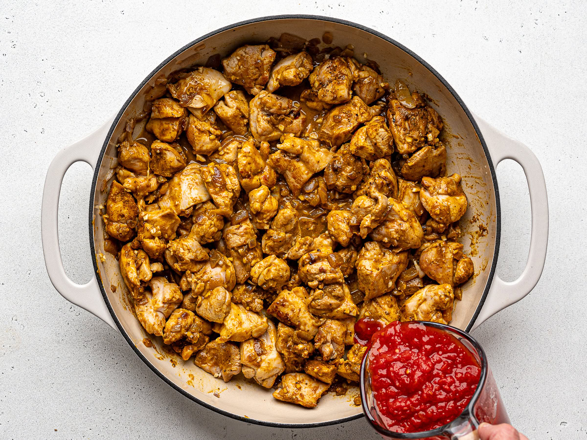 Pouring chopped tomatoes over chicken mixture.