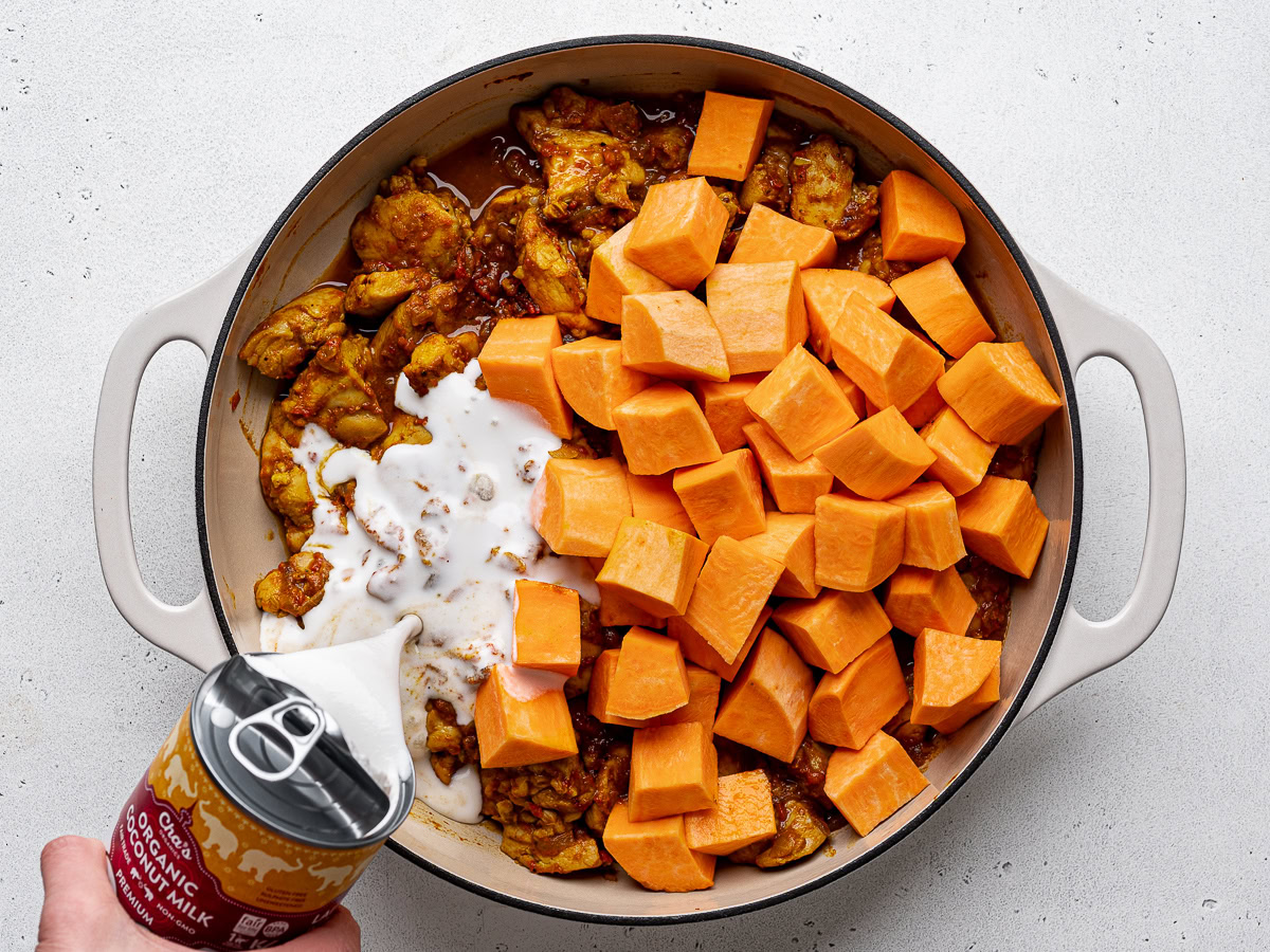 Pouring coconut milk over sweet potato chunks and chicken mixture.