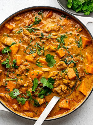 Cooked chicken sweet potato curry in a large skillet garnished with chopped cilantro.