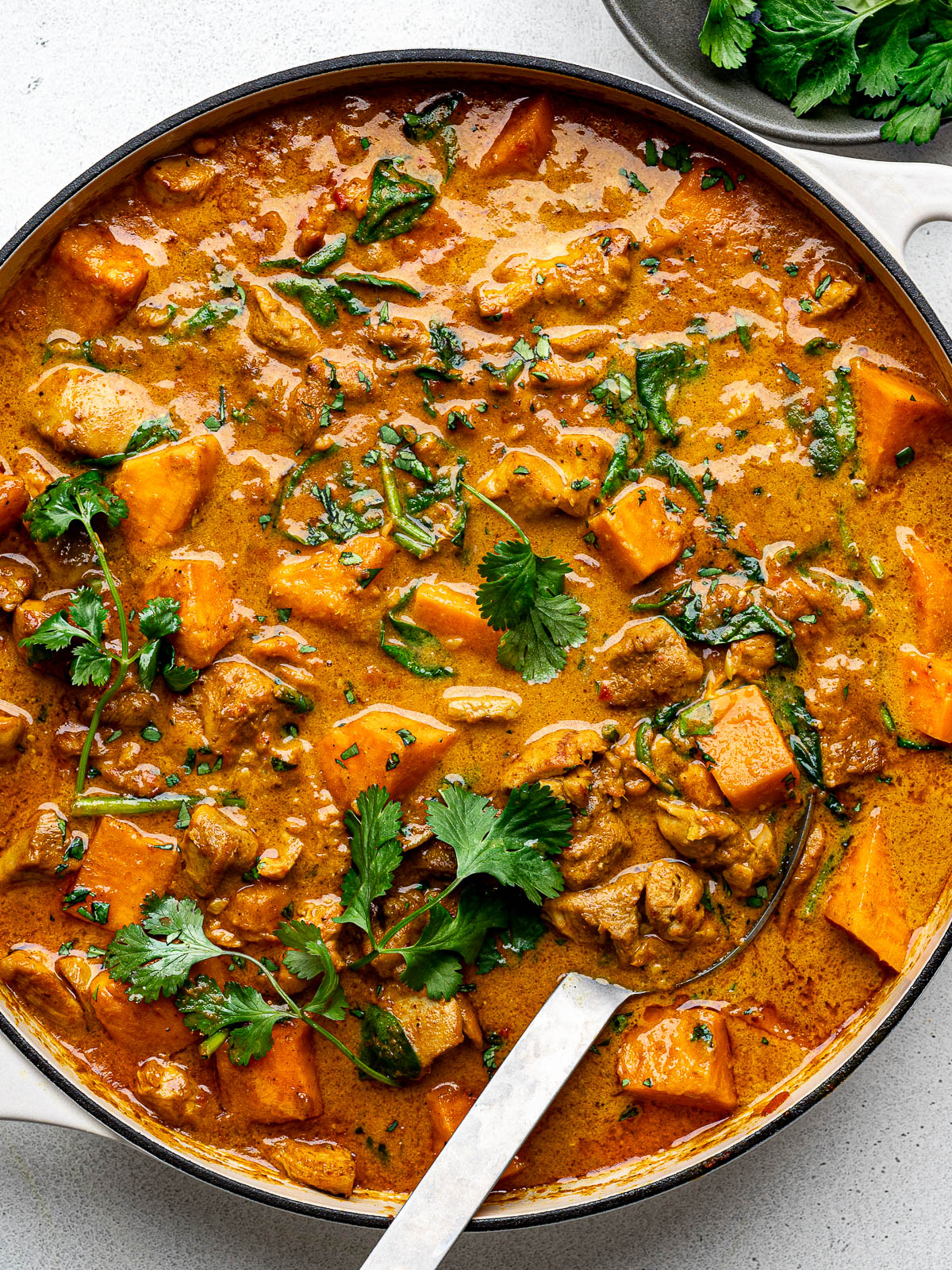 Cooked chicken sweet potato curry in a large skillet garnished with chopped cilantro.
