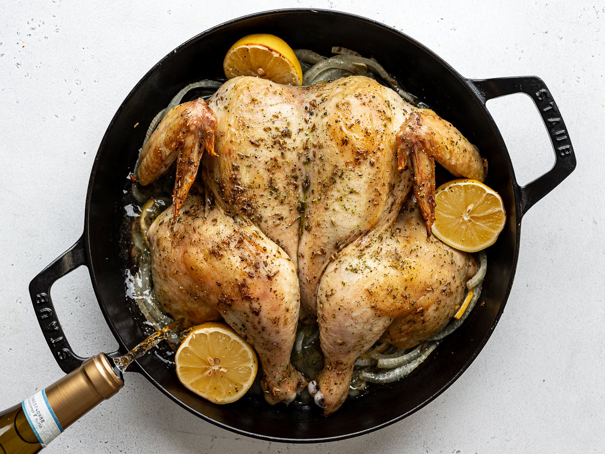 Pouring white wine around the partially-roasted chicken. 