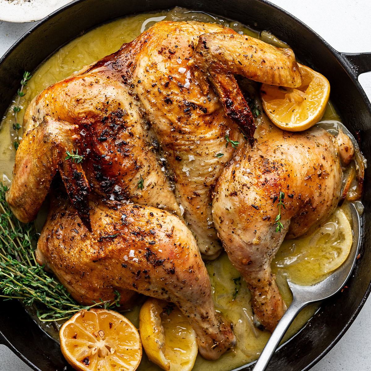 Roasted spatchcocked chicken in black skillet with roasted lemon halves and fresh thyme.