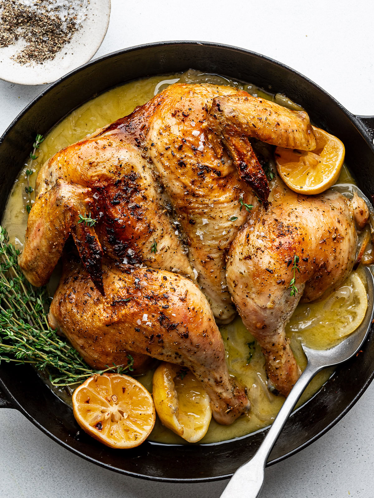 Roasted spatchcocked chicken in black skillet with roasted lemon halves and fresh thyme.