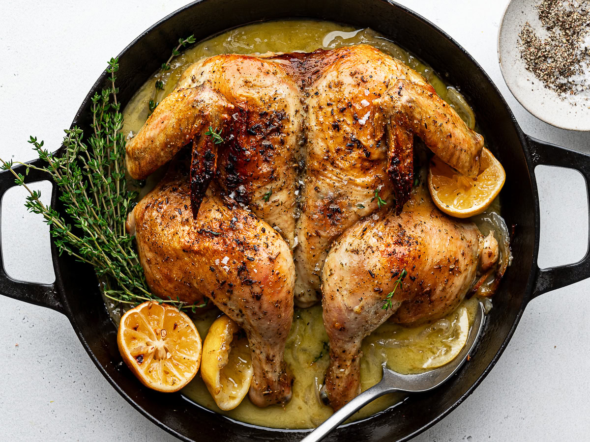 Roasted spatchcocked chicken in black skillet with roasted lemon halves and fresh thyme.