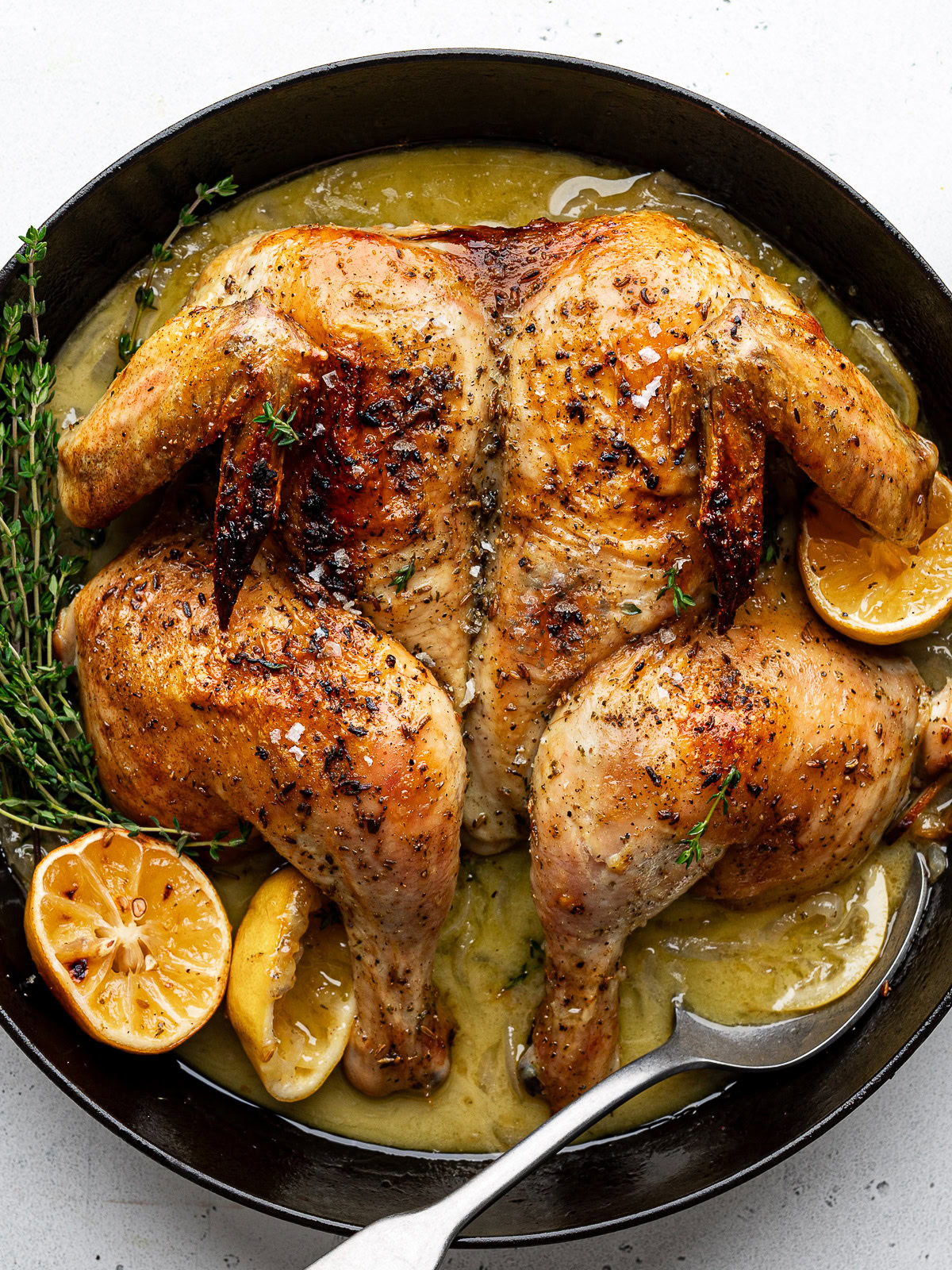 Close-up of Roasted spatchcocked chicken in black skillet with roasted lemon halves and fresh thyme.