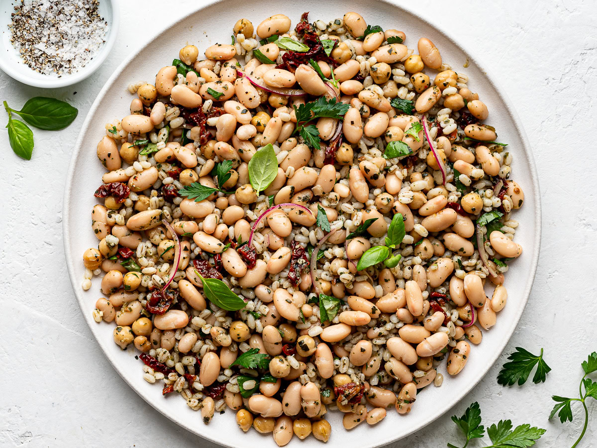 Tuscan bean salad served on a round white platter, garnished with fresh parsley and basil.