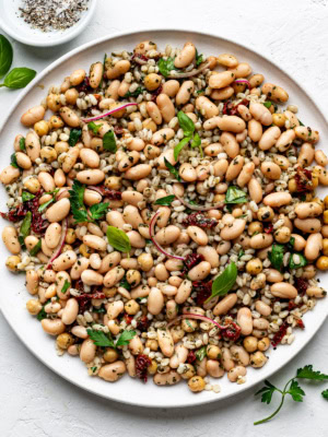 Tuscan bean salad served on a round white platter, garnished with fresh parsley and basil.