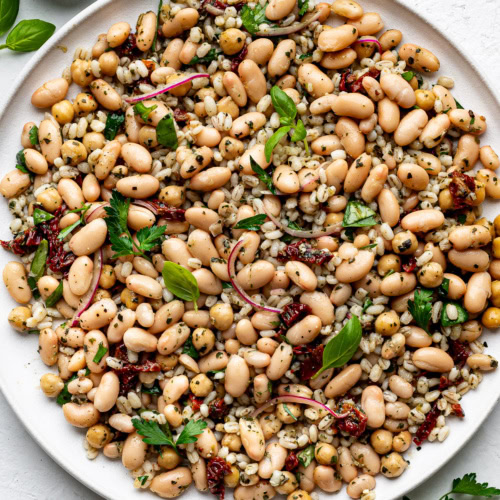 Tuscan bean salad served on a round white platter, garnished with fresh parsley and basil.
