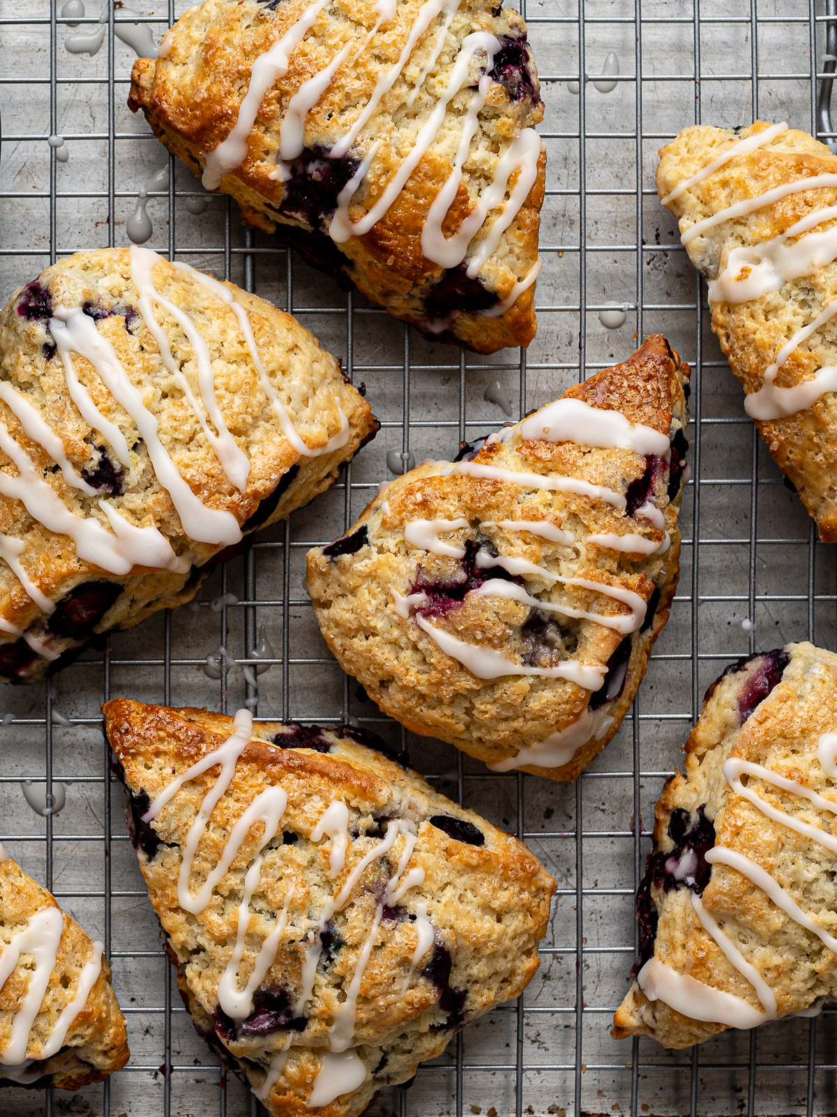 Close up of baked scones drizzled with glaze on baking sheet rack.