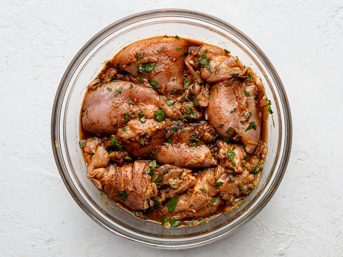 Chicken thighs marinating in a glass bowl.