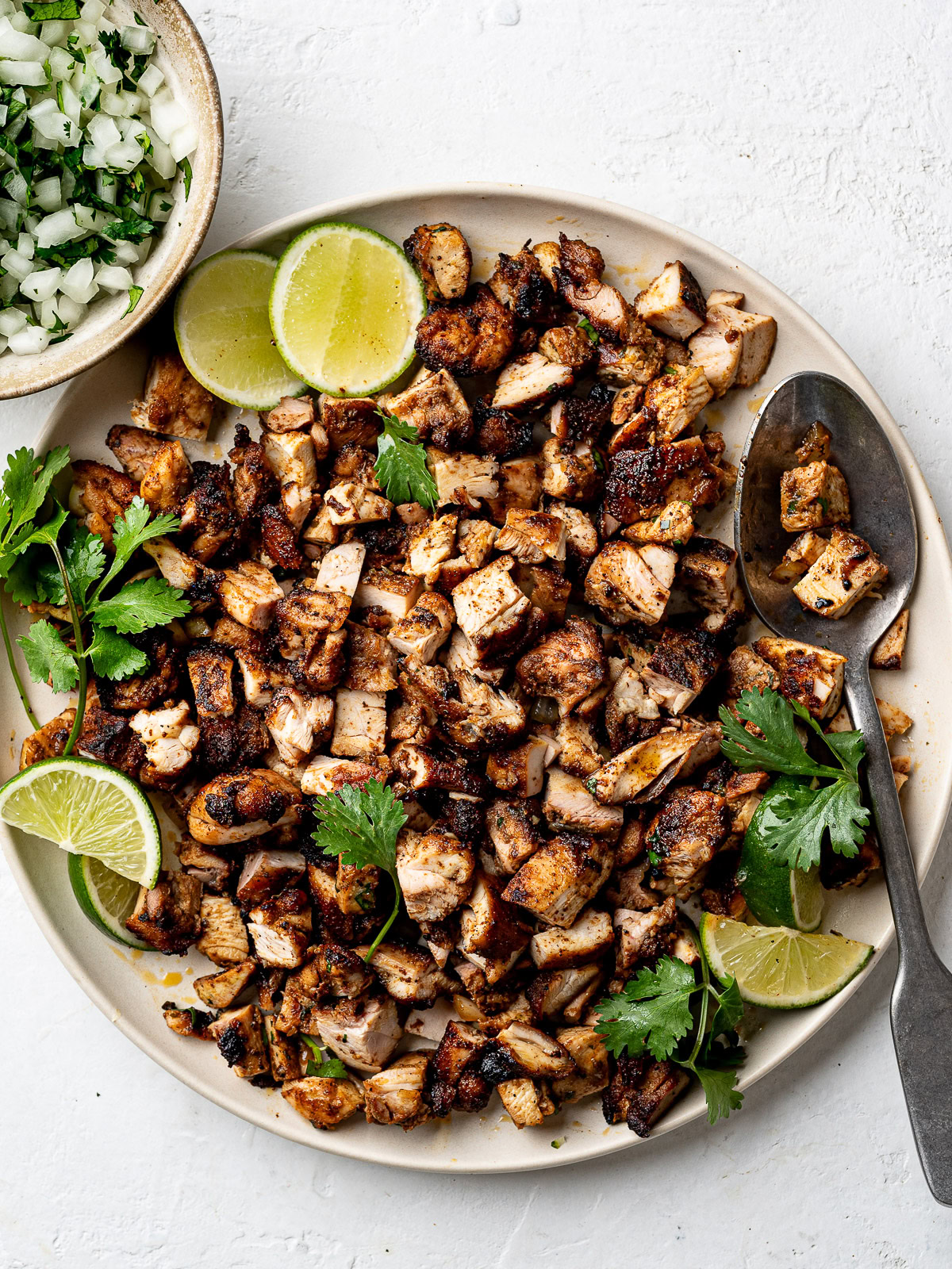Chopped grilled chicken for street tacos on a large platter with a bowl of diced onion and cilantro on the side. 