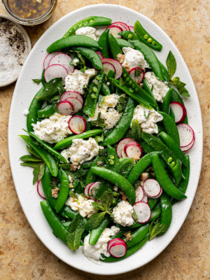 Sugar snap pea and burrata salad served on an oval white platter.