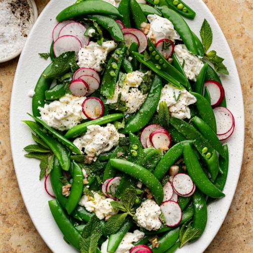 Sugar snap pea and burrata salad served on an oval white platter.