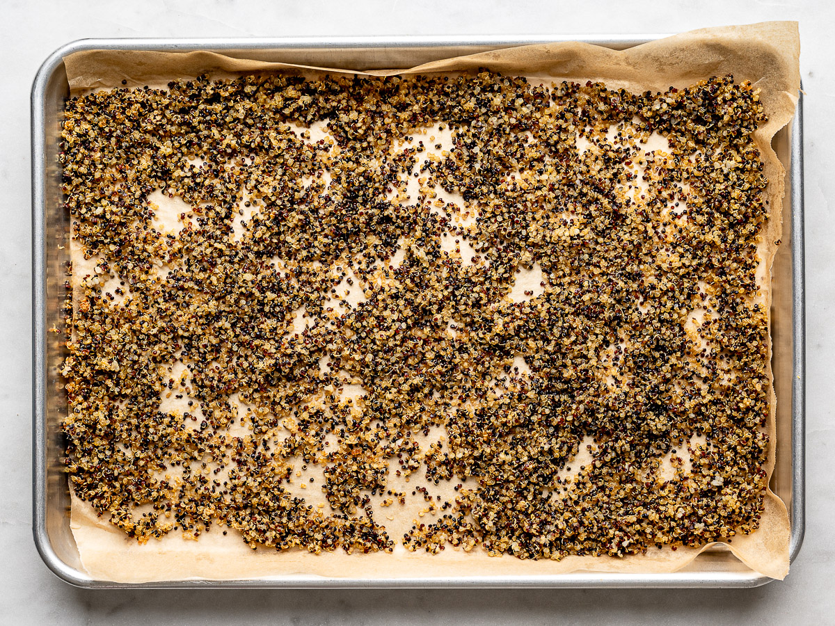 Crispy quinoa spread out on parchment-lined baking sheet. 