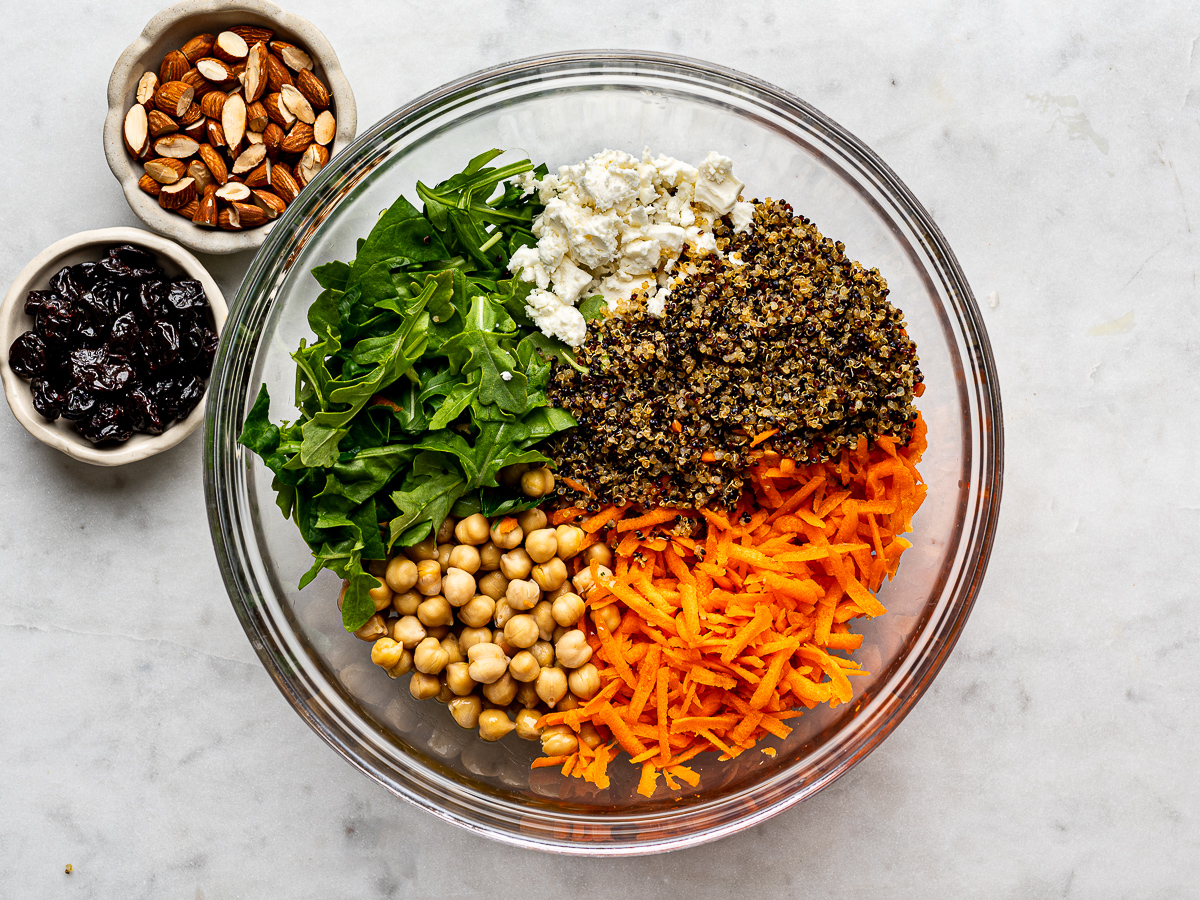 Salad ingredients in glass bowl with small bowls of almonds and dried cherries on the side.
