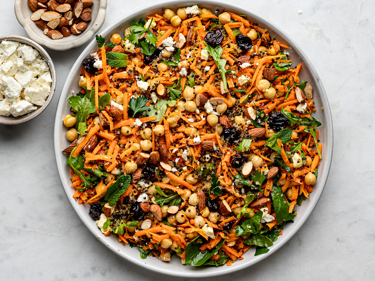 Carrot Salad with crispy quinoa served on a large round platter with small bowls of almonds and crumbled feta on the side.