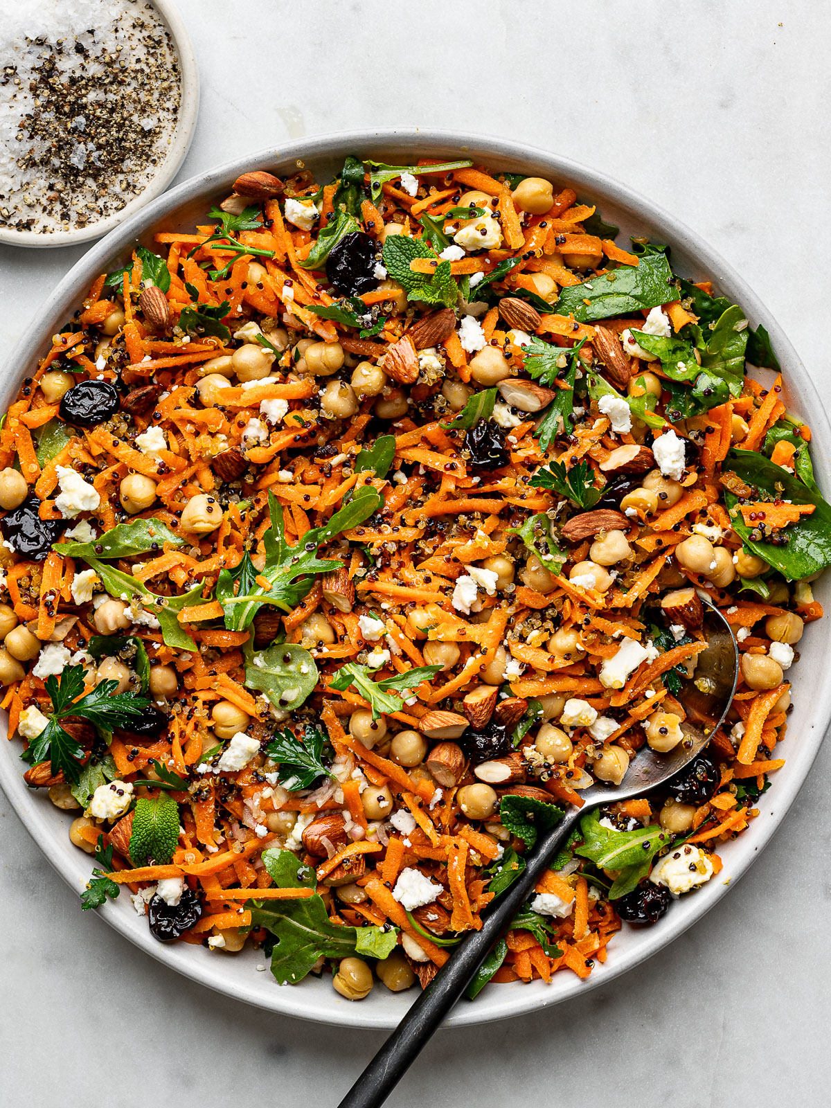 Carrot Salad with crispy quinoa served on a large round platter with small salt and pepper pinch dish on the side.