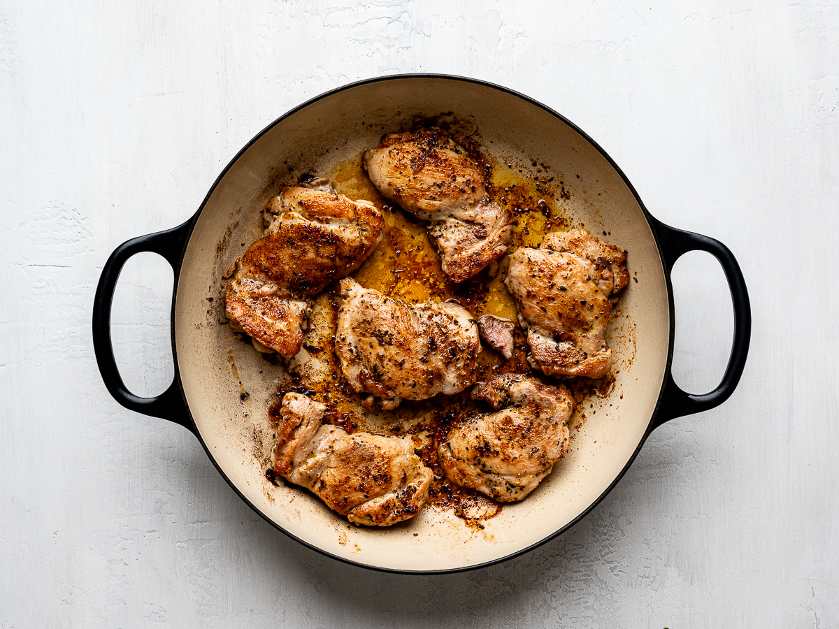 6 browned chicken thighs in black skillet. 