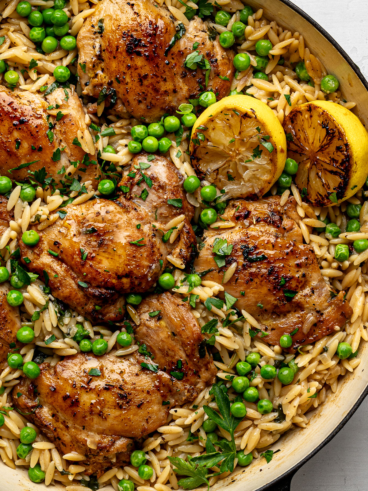 Close up of One-Pan Chicken And Lemon Orzo in black skillet with two charred lemon halves.