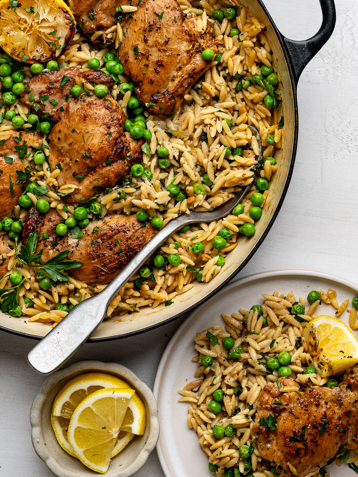 One-Pan Chicken And Lemon Orzo in black skillet a small white plate with a serving of the chicken and orzo dish. 