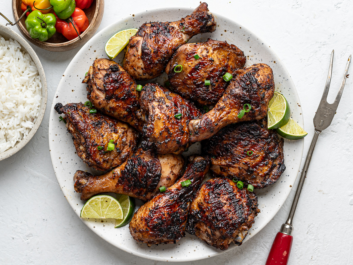 Jerk-spiced chicken served on a round platter with a small bowl of scotch bonnets on the side as props and side bowl with white rice. 