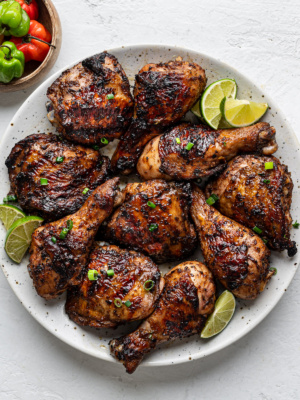 Jerk-spiced chicken served on a round platter with a small bowl of scotch bonnets on the side as props.