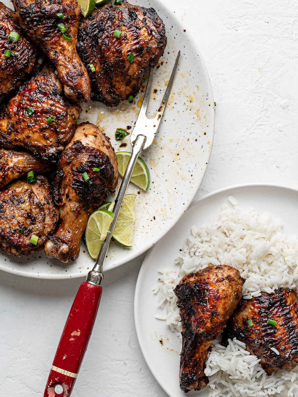 Jerk-spiced chicken pieces served on a round platter and a small plate with white rice and two chicken pieces. 
