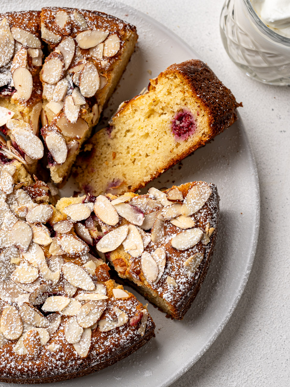Close up of Raspberry Almond Ricotta Cake on a white platter with one sliced piece flipped to show the inside crumb.