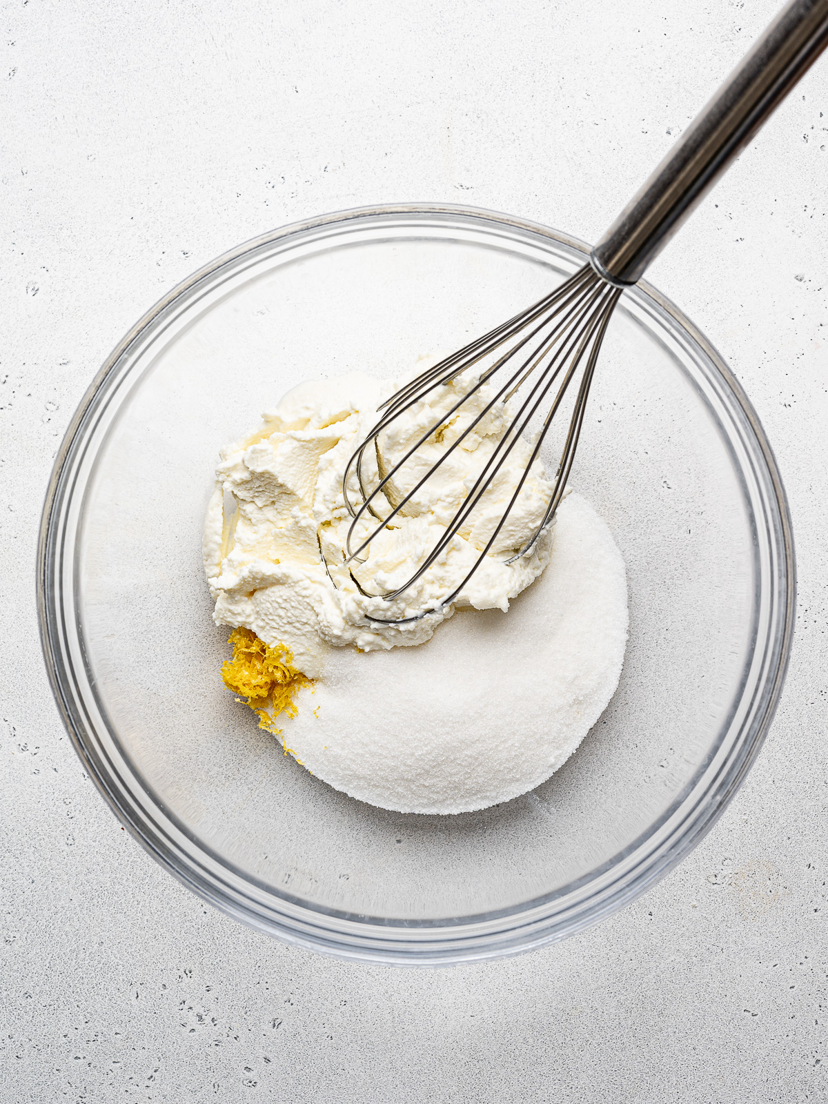 Mixing ricotta cheese, lemon zest and sugar in glass mixing bowl.
