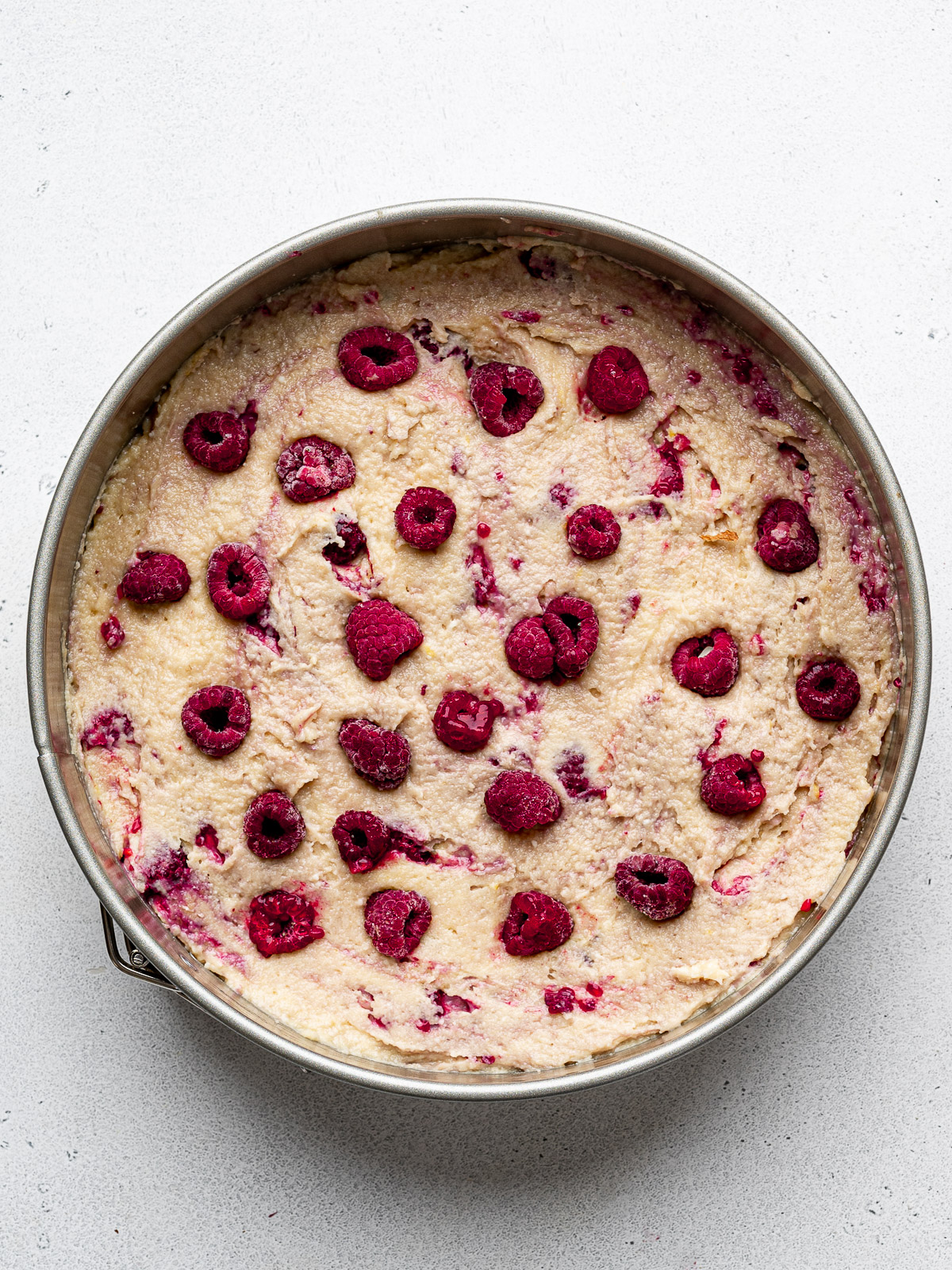 Cake batter in springform pan dotted with frozen raspberries on top.