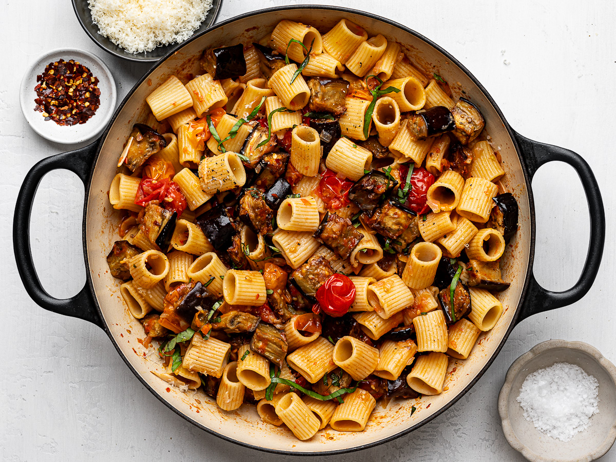 Roasted eggplant pasta in skillet with bowls of cheese, salt and pepper on the side.  