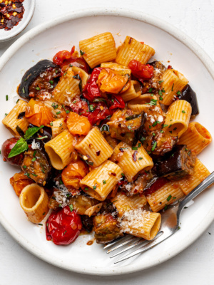 Roasted eggplant pasta served on a white plate garnished with fresh basil.