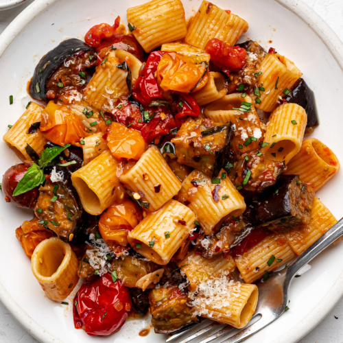 Roasted eggplant pasta served on a white plate garnished with fresh basil.
